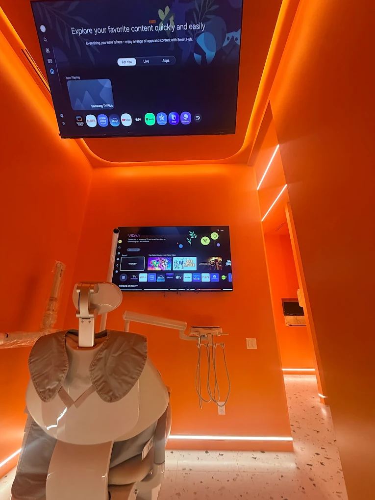 Orange-lit Dandy Dental treatment room with a dental chair and ceiling-mounted TV